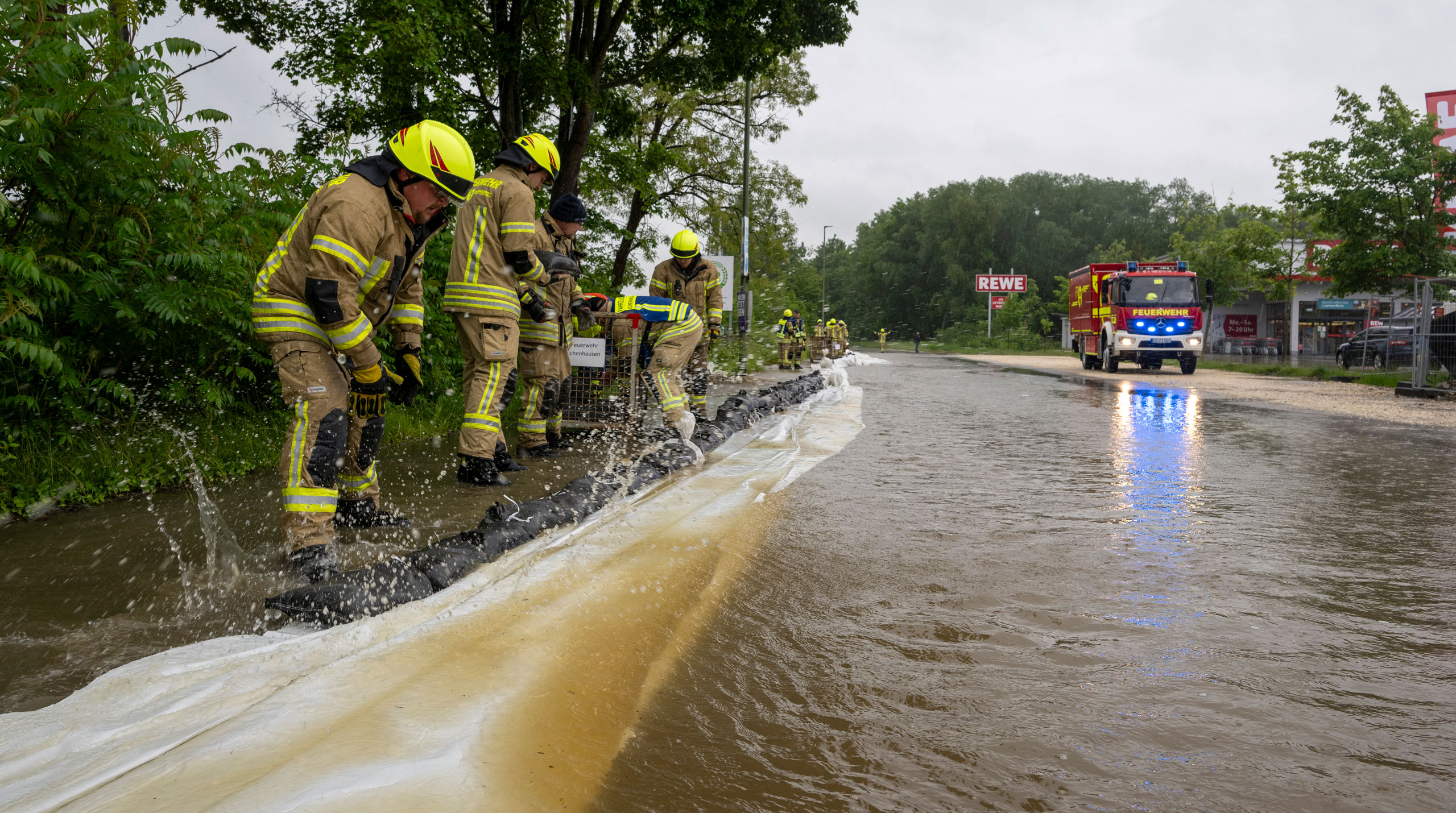 Feuerwehrleute arbeiten an einer von der Günz überfluteten Straße in Ichenhausen, um das Wasser aus der Stadt fernzuhalten. 