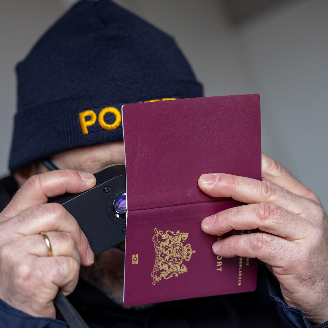 ein Polizist mit einer Lupe der einen Reisepass genau mit der Lupe überprüft