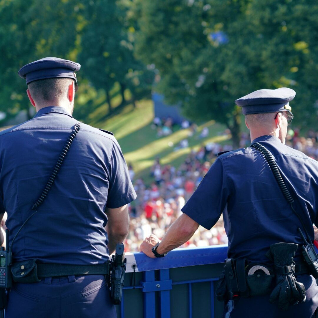 Auf dem Bild sind zwei Polizisten auf einer Brücke zu sehen, wie diese die Besucherströme bei einer Veranstaltung beobachten