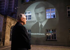 Herrmann blickt zur Projektion von Anton Fliegerbauer an der Wand der Polizeiinspektion
