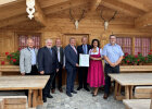 Gruppenfoto mit eingerahmter Auszeichnung vor Holzhaus mit Tischen und Bänken