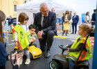 Innenminister Joachim Herrmann kniet zu Kindern in Verkehrswarnfesten auf Bobycars