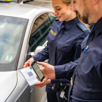 Polizistin und Polizist beim Scannen des QR-Codes des Strafzettels mit dem Handy 