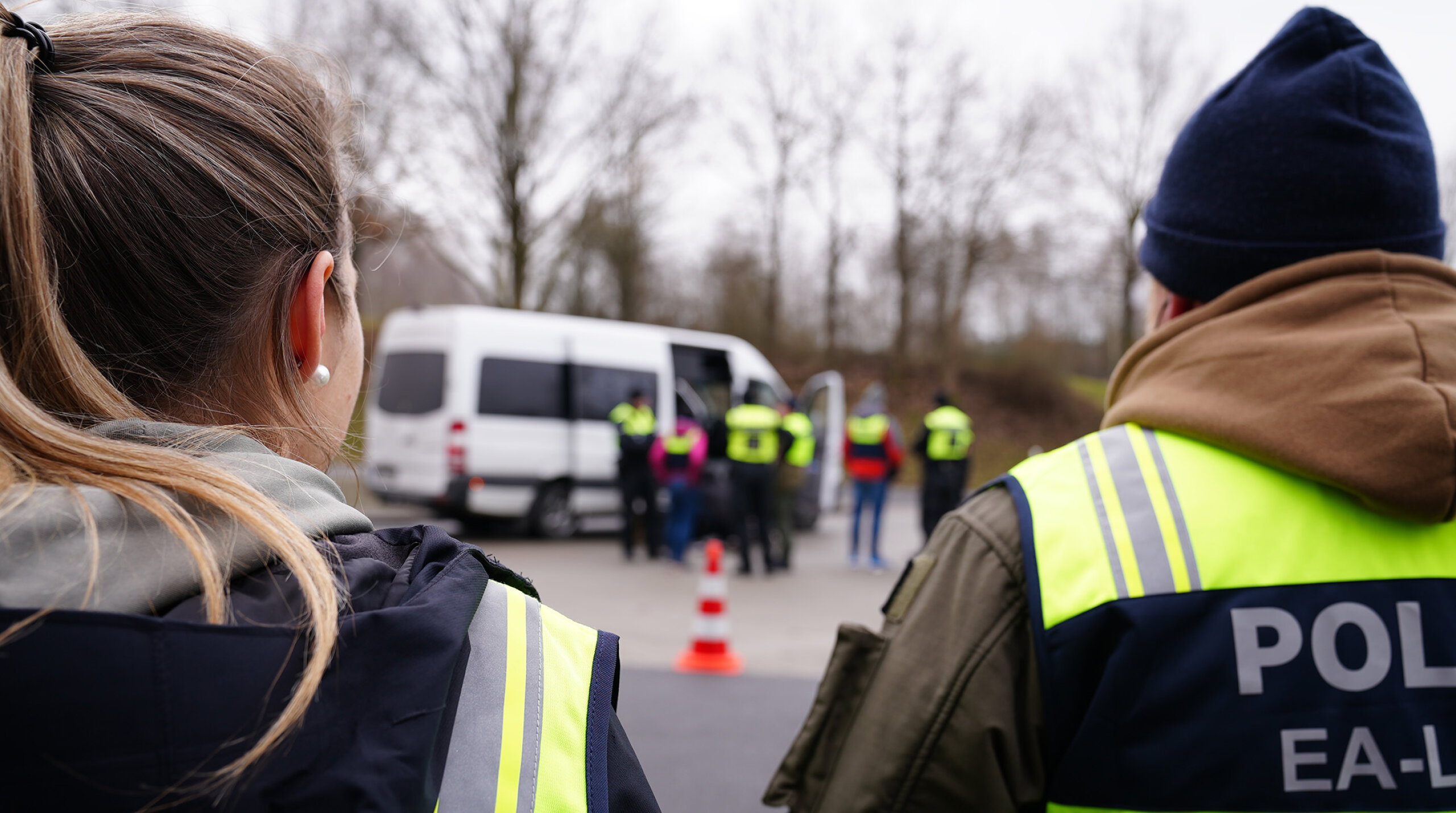 zwei Polizist*innen von hinten mit Warnweste, im Hintergrund Kontrolle eines Vans