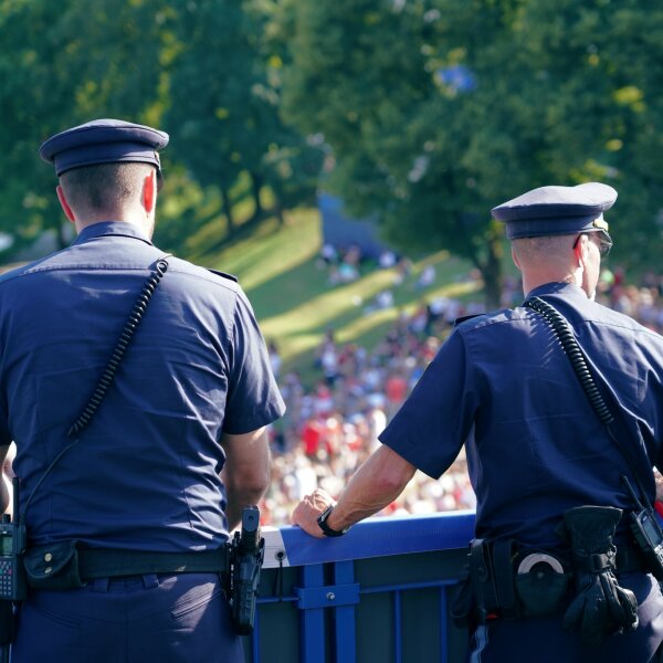 Auf dem Bild sind zwei Polizisten auf einer Brücke zu sehen, wie diese die Besucherströme bei einer Veranstaltung beobachten