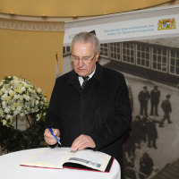 Innenminister Herrmann trägt sich in ein Gästebuch der Ausstellung ein