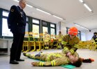 Kinder in Feuerwehrkleidung bei Übung in Klassenraum, daneben Dozent in Feuerwehruniform