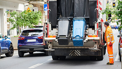 Müllmann lädt eine blaue und eine schwarze Mülltonne in den Müllwagen