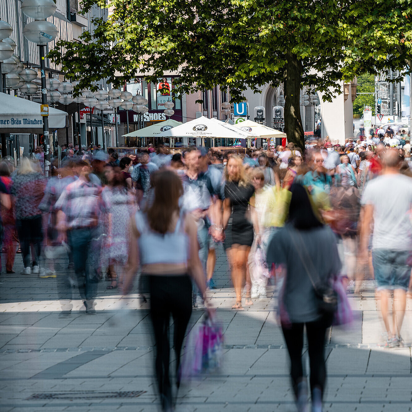 523256111 Passanten sind von vorne und hinten in der Münchner Fußgängerzone zu sehen. Im vorderen Bildbereich sind die Personen unscharf abgebildet.