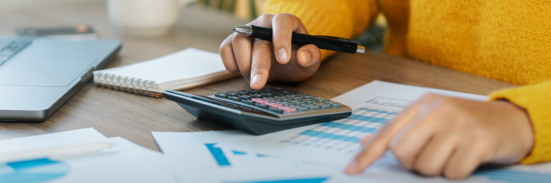 Frau gibt Zahlen in einen Taschenrechner ein, neben ihr auf dem Tisch einige Papierunterlagen